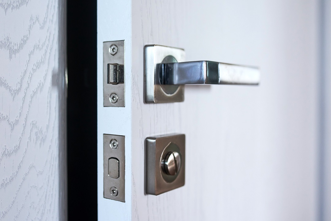 Close-up of a room door with a handle and a metal lock