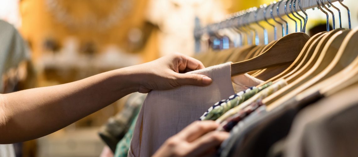 Close up of woman hand choosing thrift young and discount t-shirt clothes in store, searching or buying cheap cotton shirt on rack hanger at flea market , stall shopping apparel fashion concept